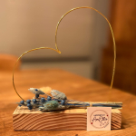 hartje in goudkleurige metaaldraad met droogbloemen in blauw- of rozetinten op steigerhouten plankje