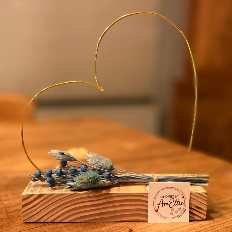 hartje in goudkleurige metaaldraad met droogbloemen in blauw- of rozetinten op steigerhouten plankje