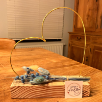 hartje in goudkleurige metaaldraad met droogbloemen in blauw- of rozetinten op steigerhouten plankje